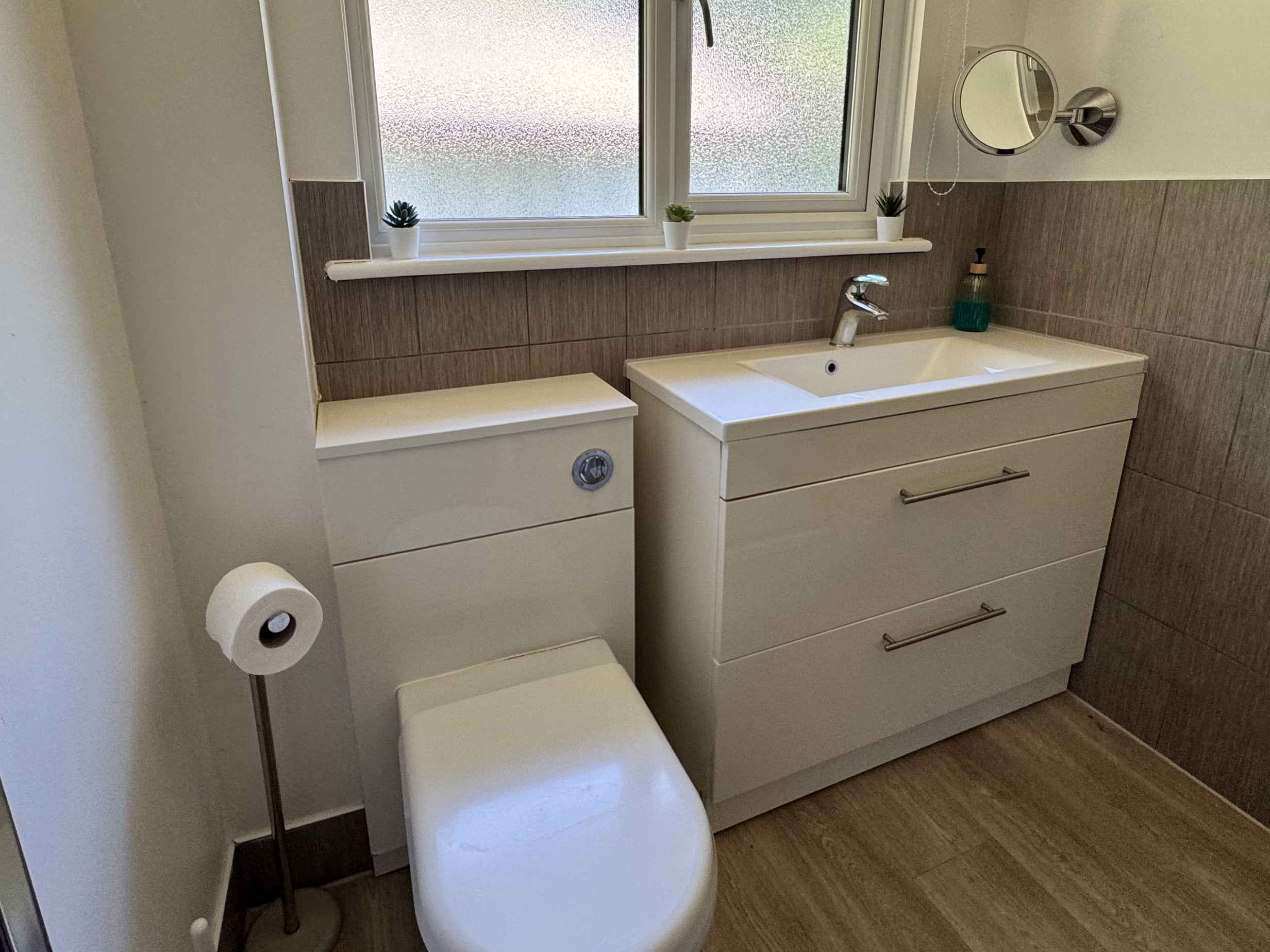 The bathroom at Bencoolen, with a WC, a basin on a white vanity unit and a frosted window over tiled walls