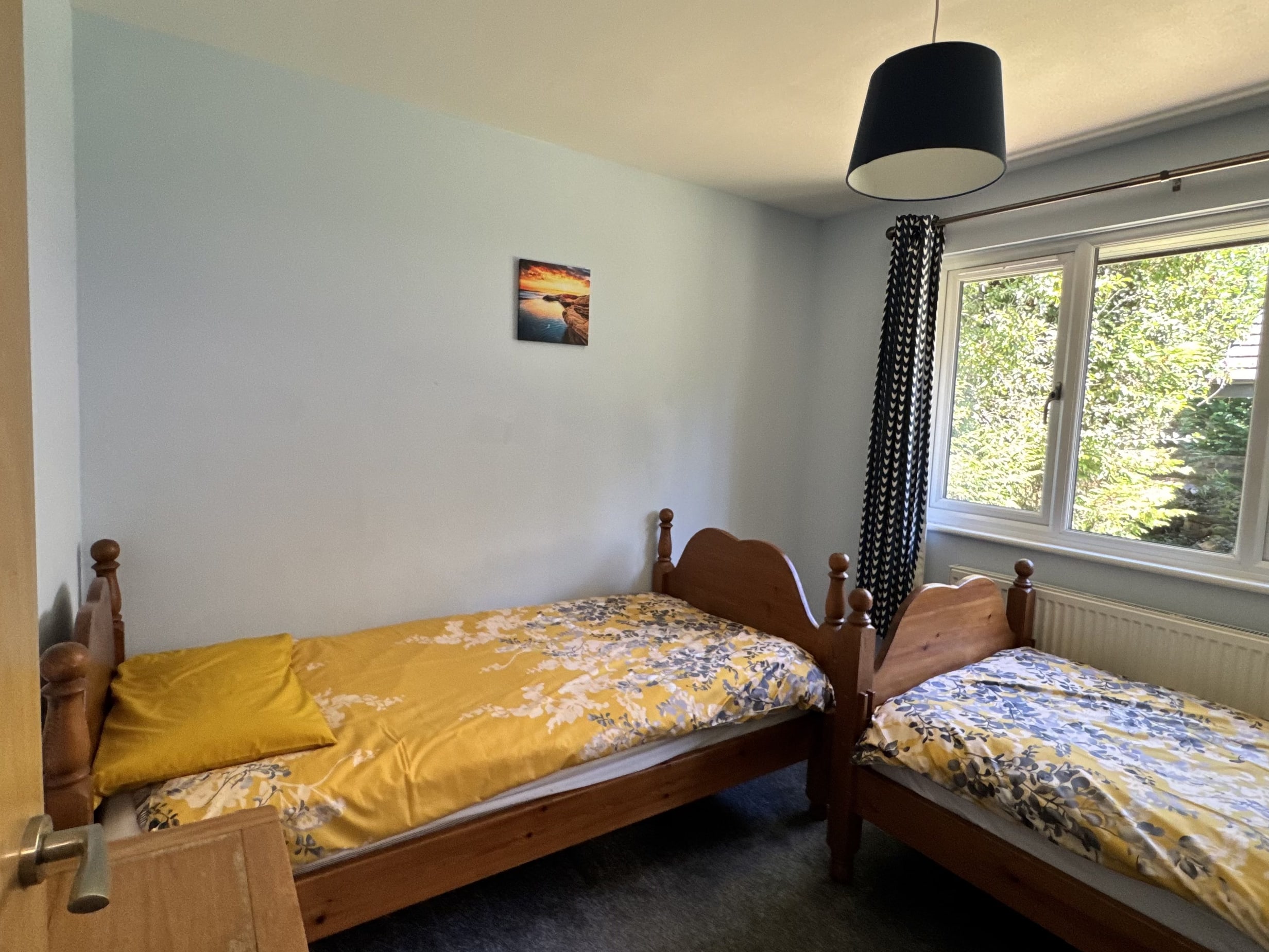 The twin bedroom at Bencoolen, with two single beds made up in yellow and blue floral bedding beside a window onto the trees