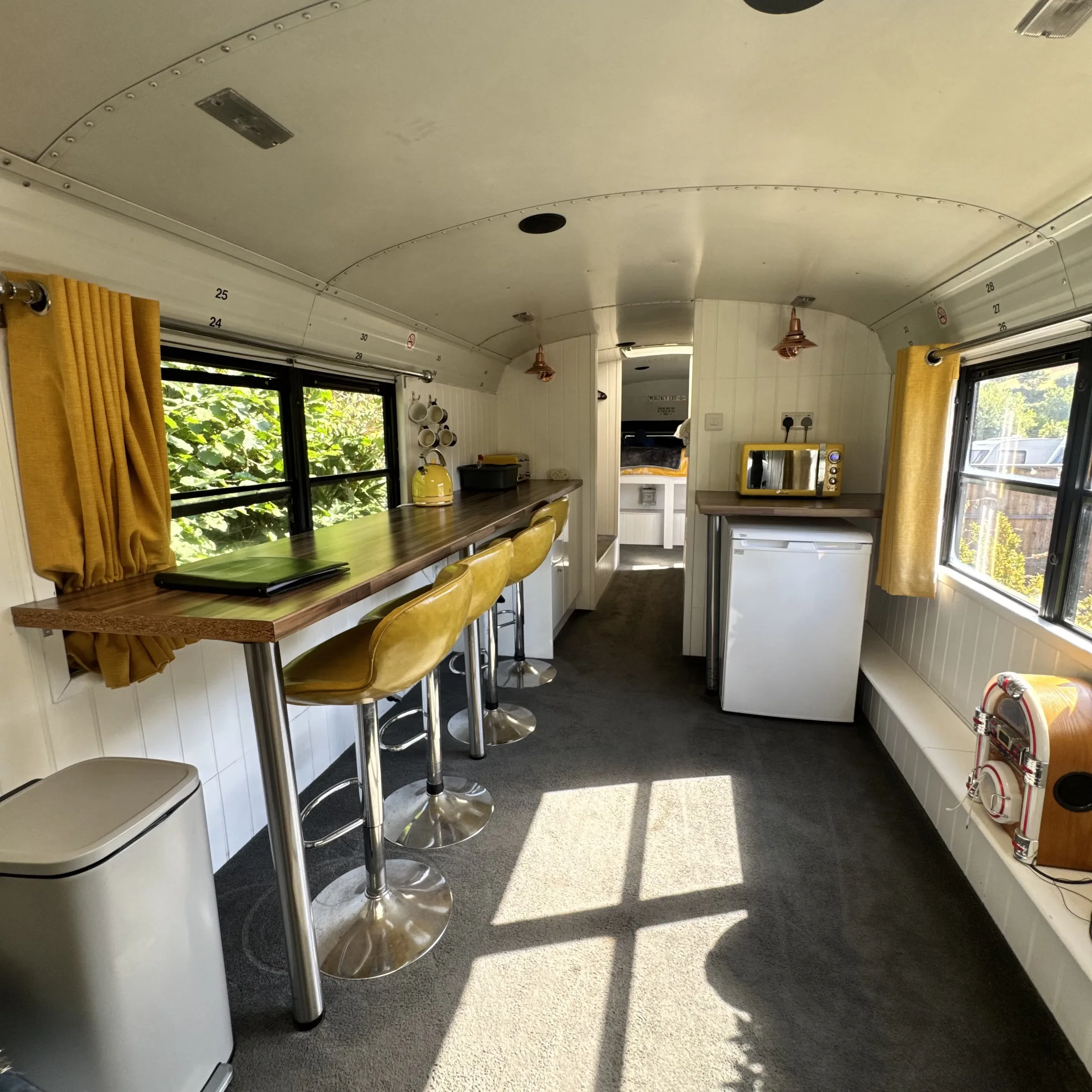 The breakfast bar running along the bus windows with yellow stools, and the fridge beyond