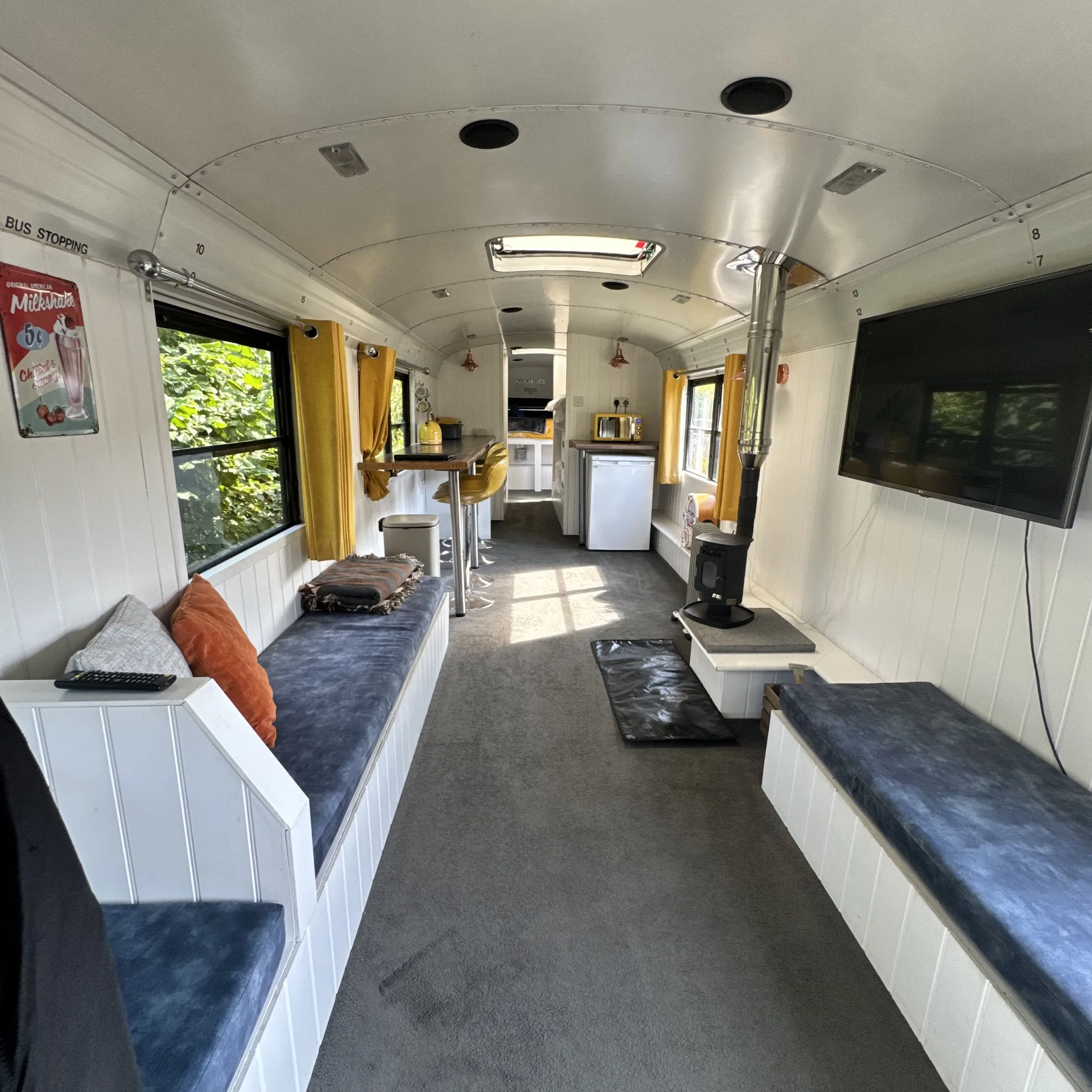 The living end of Bluebird, with bench seating either side, the log burner and a wall-mounted TV