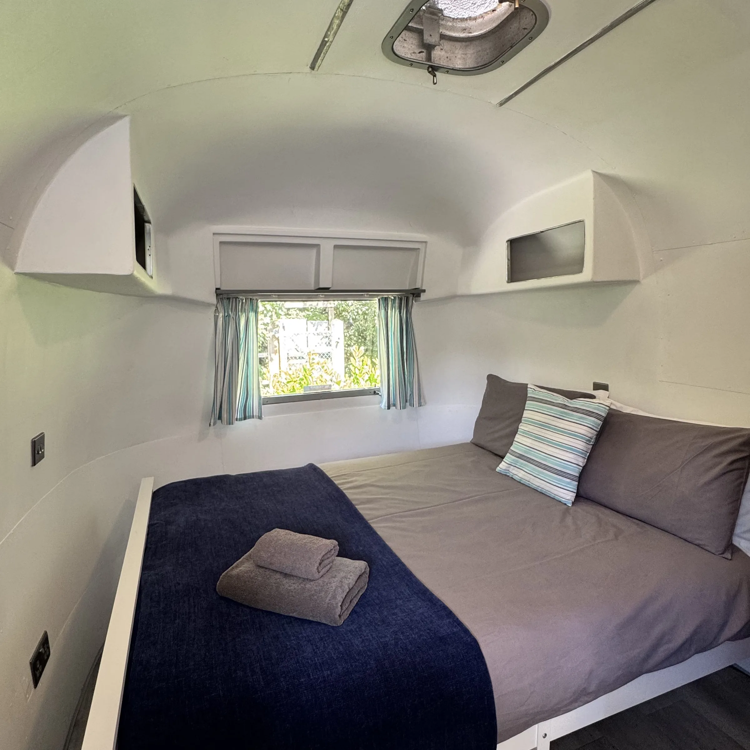 The made-up bed inside Boskenna, with folded towels and a curtained window