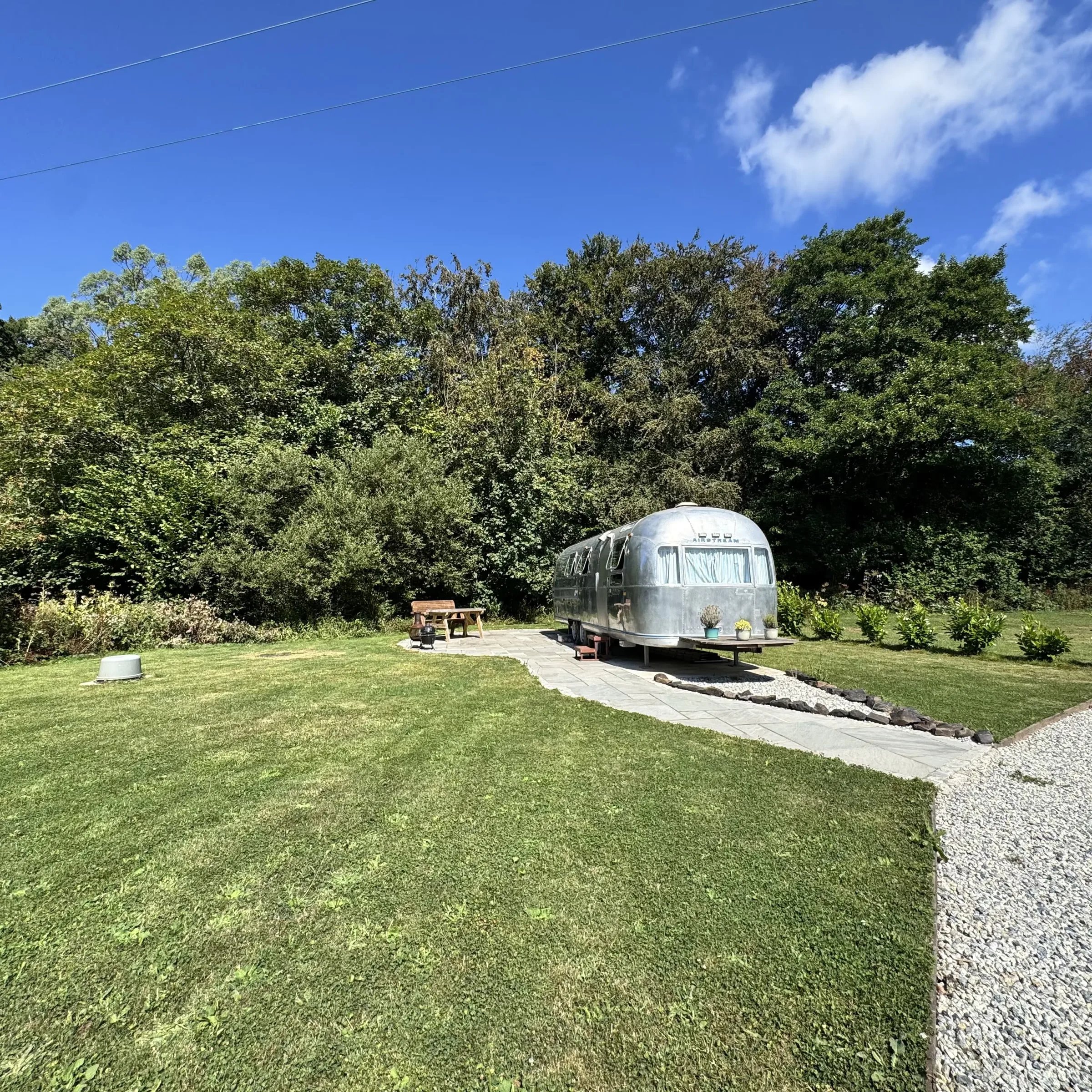 Boskenna seen across the grass, with the Airstream and its picnic bench set against the trees