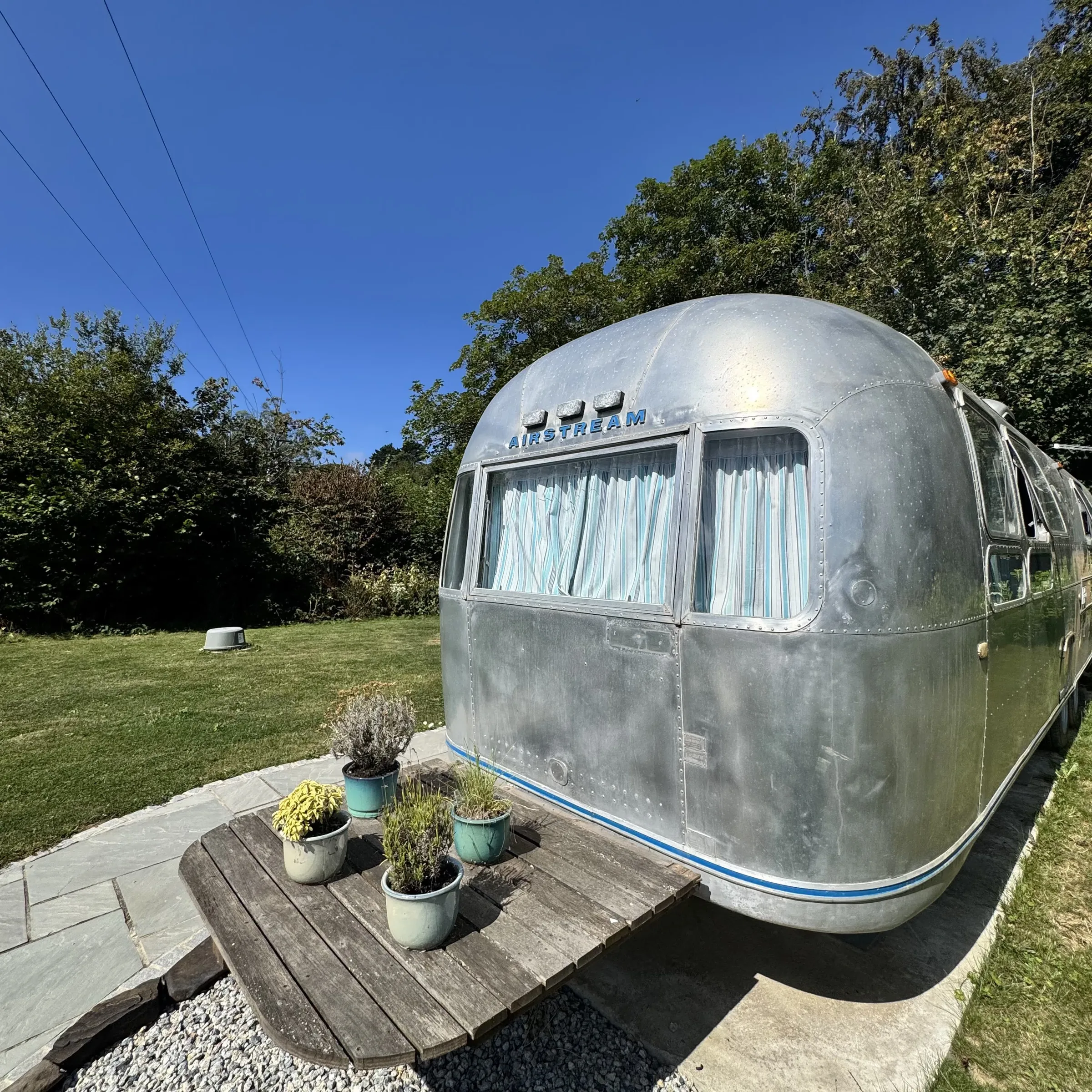 The curved aluminium nose of the Airstream at Boskenna, with potted plants alongside