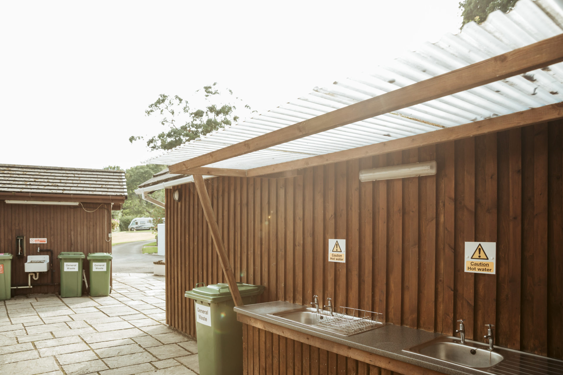 The covered washing-up area, two stainless steel sinks under a timber lean-to with the bins opposite