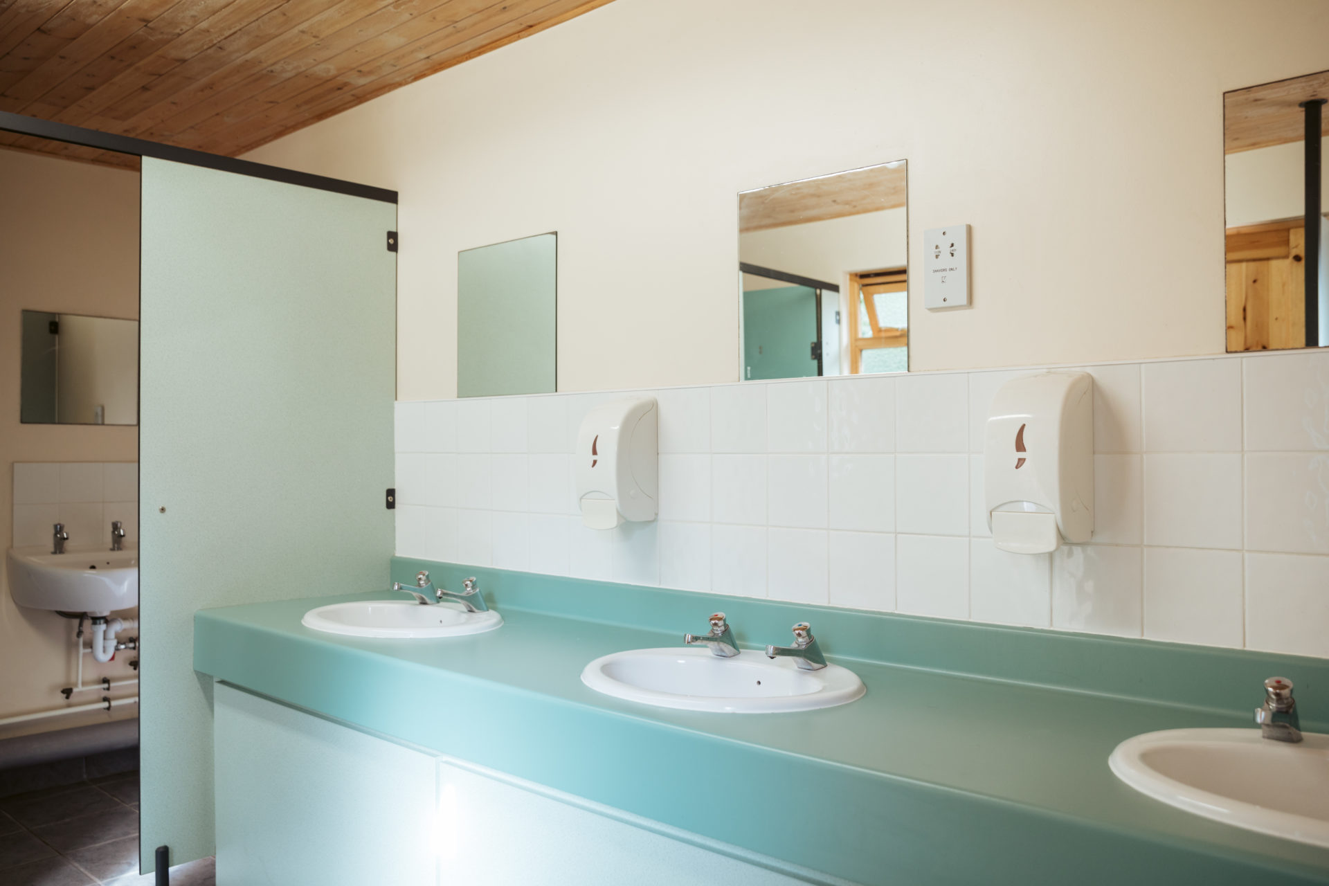 Inside one of the washrooms: a row of basins along a mint-green counter under wall mirrors, white tiling and a pine-boarded ceiling