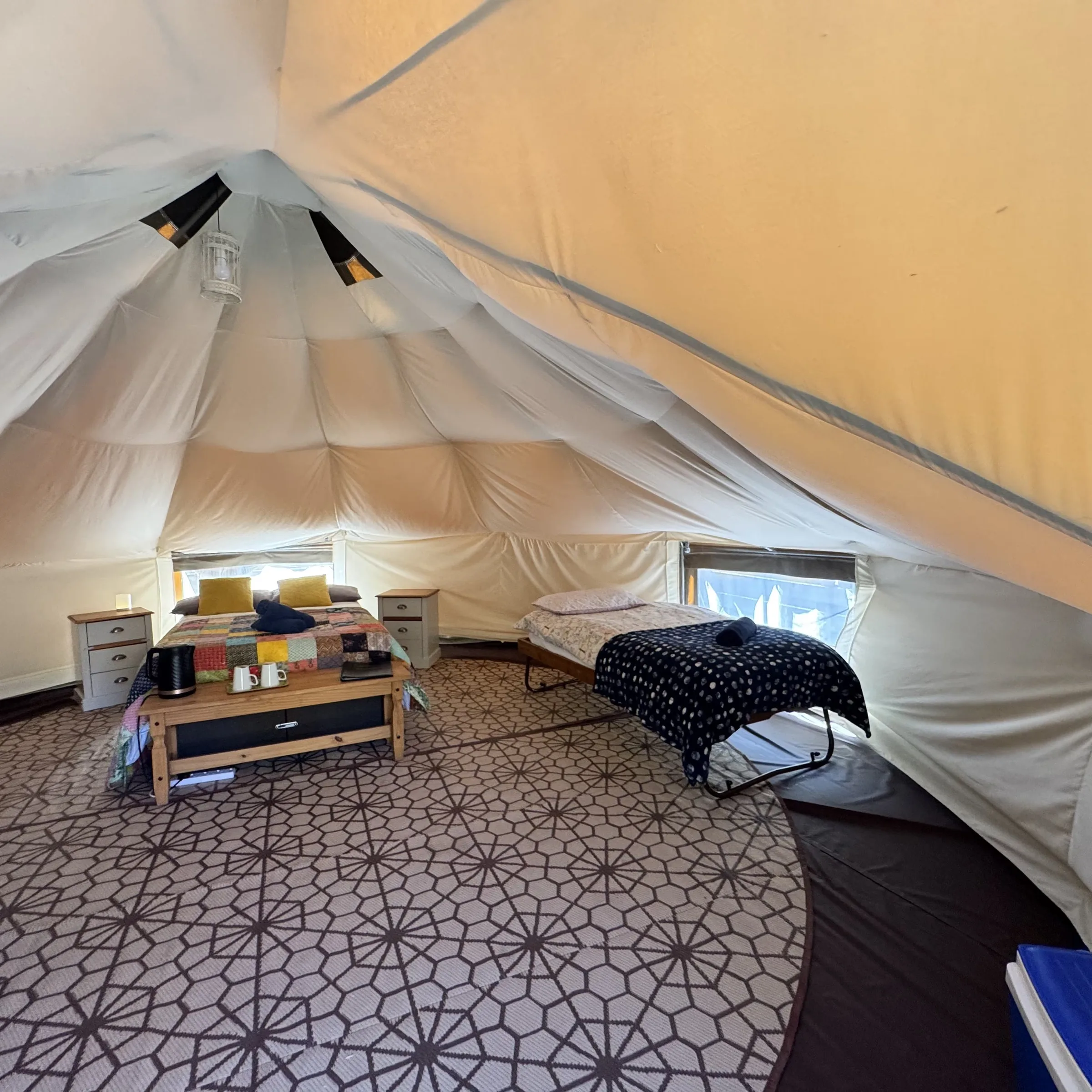 Inside Hartland’s bell tent: the double bed with a single bed either side, matting underfoot and a low table with a kettle and guest folder