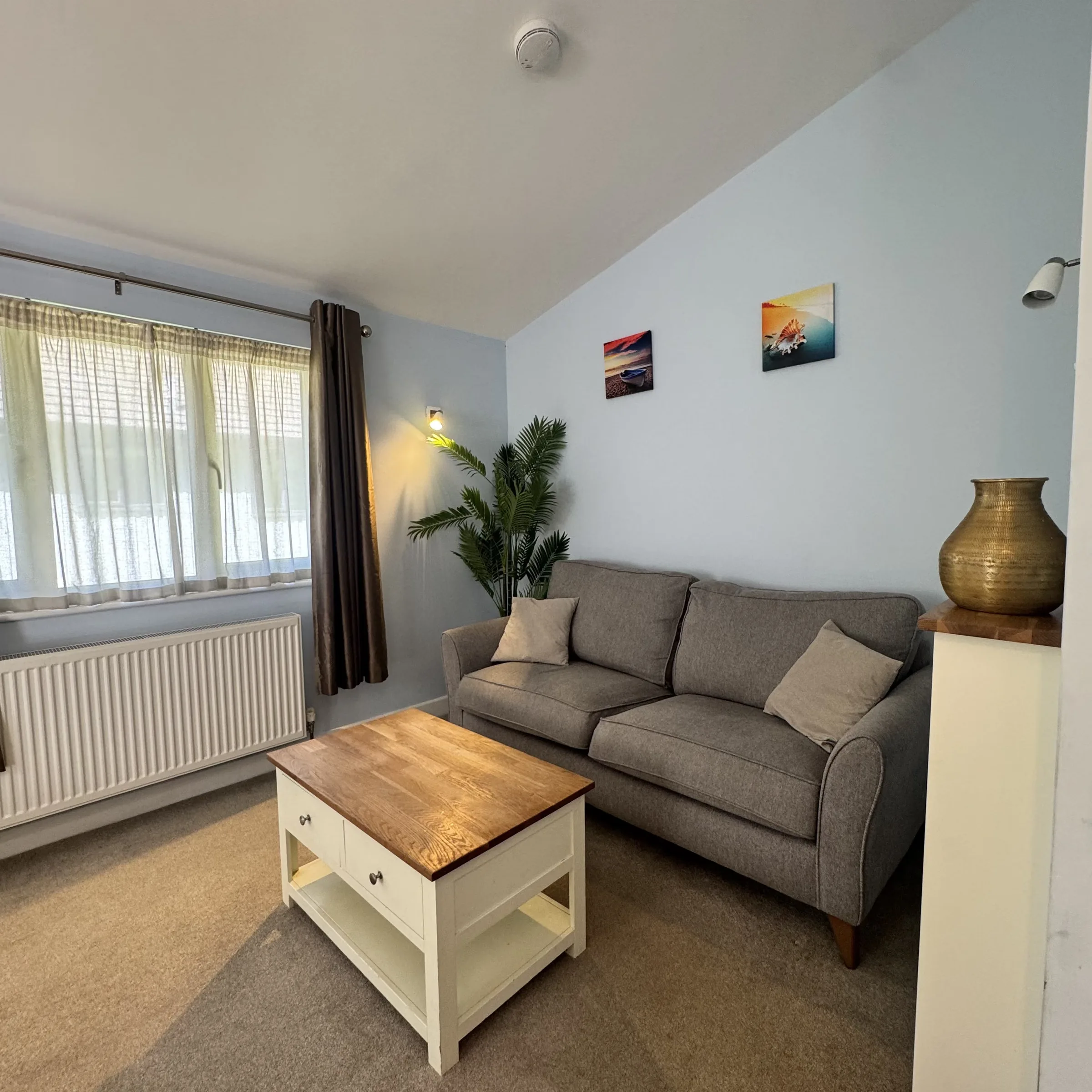 The sitting area at Heath, with a sofa, oak coffee table and coastal prints on the wall