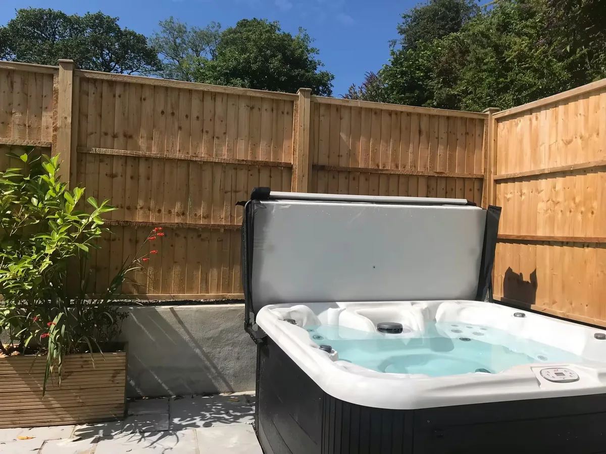 A lodge hot tub with its cover propped open on a paved terrace at Helyk