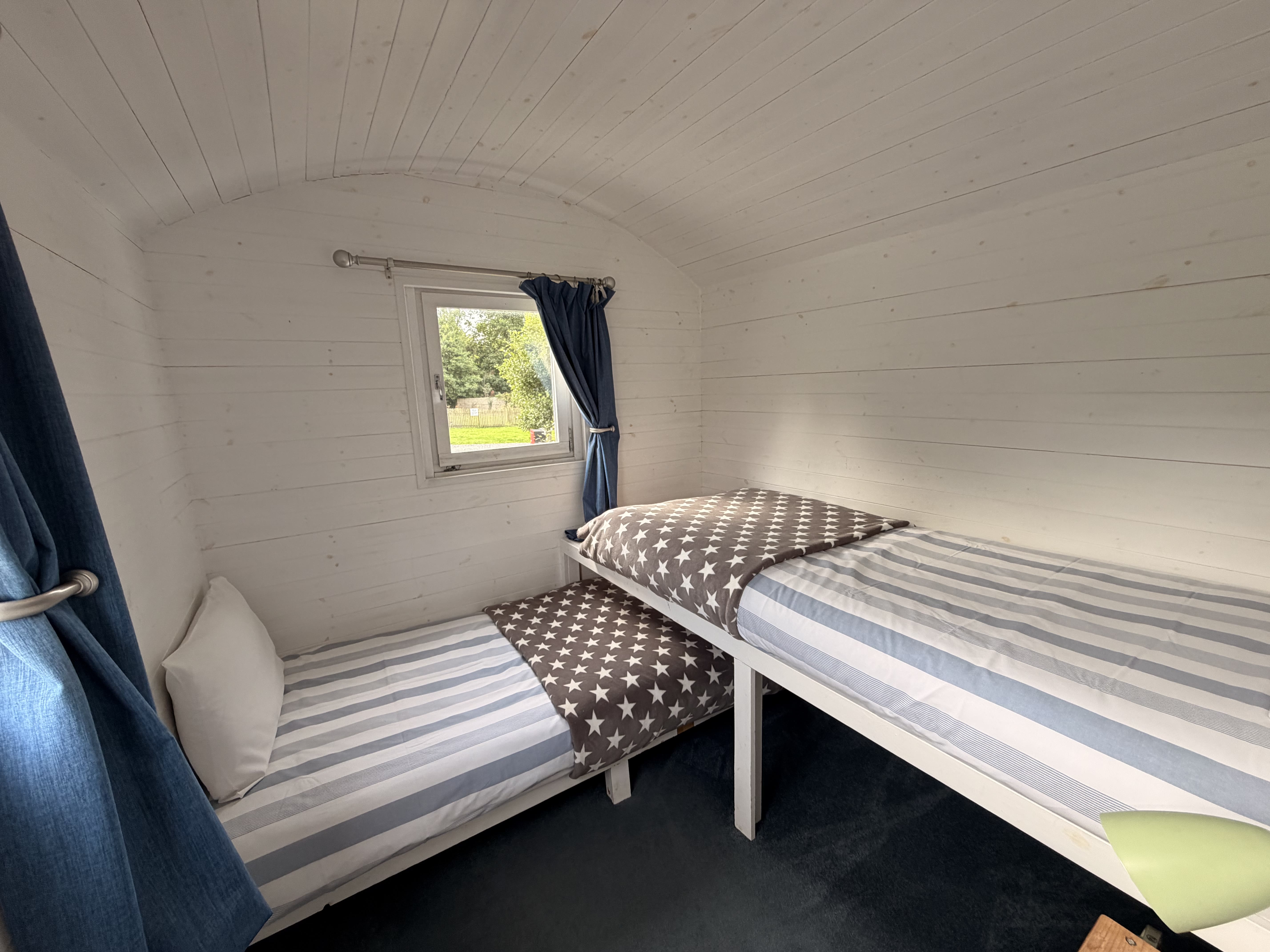 The two single beds in their own small room at the end of the hut, made up with striped bedding and star-print throws beneath the curtained window