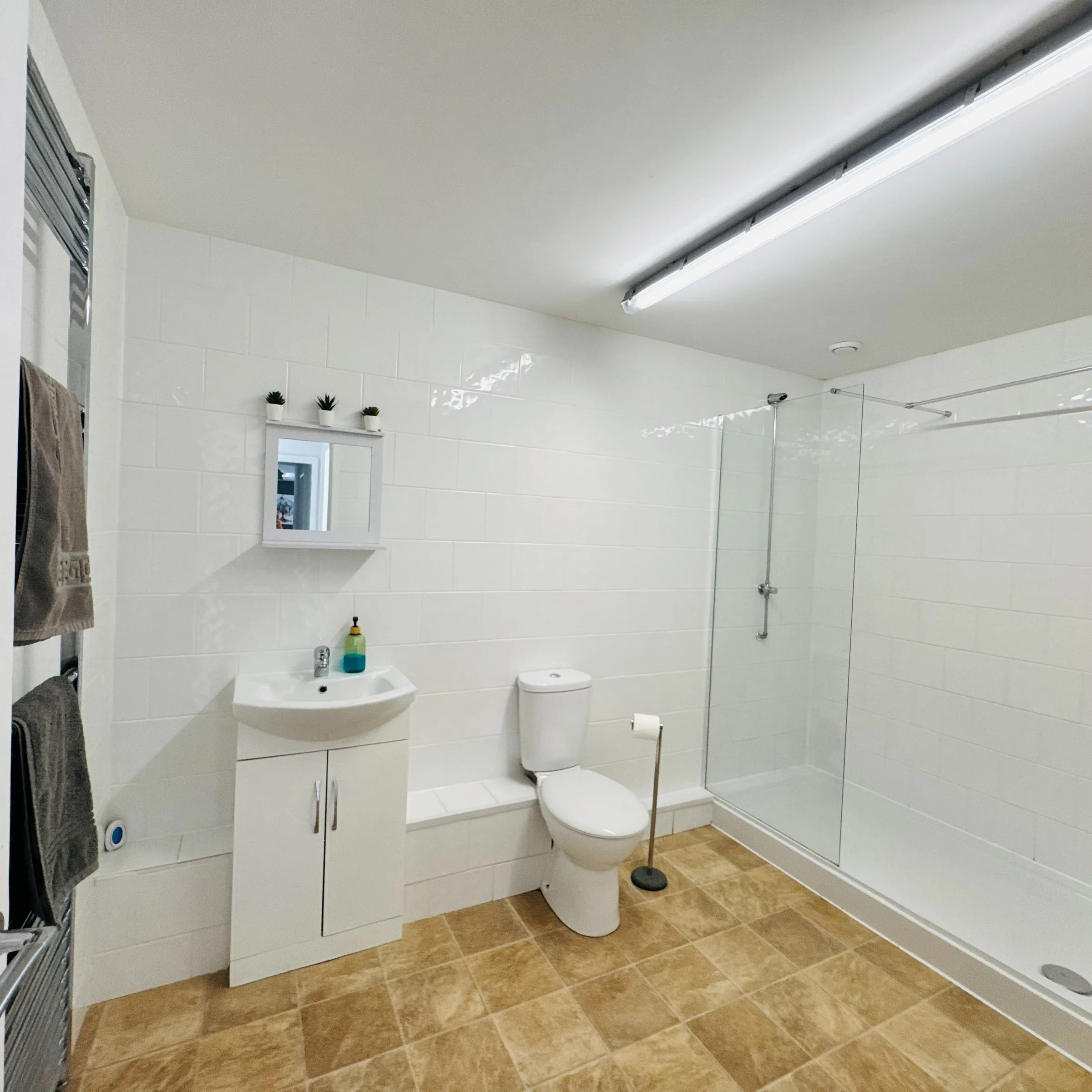A Mordros bathroom with a bath, glass shower screen, and a wall-mounted sink beneath a mirrored cabinet