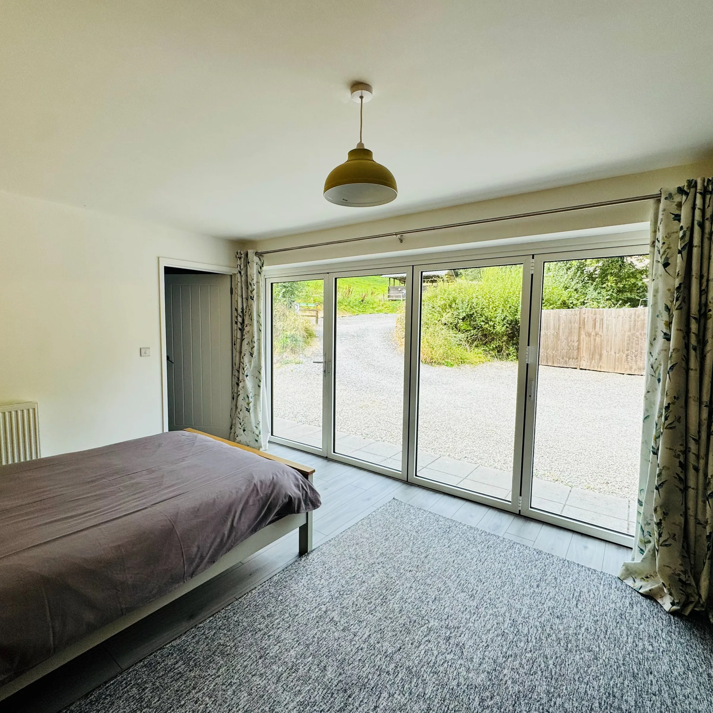 A ground-floor Mordros bedroom with full-width sliding doors opening straight onto the gravel drive