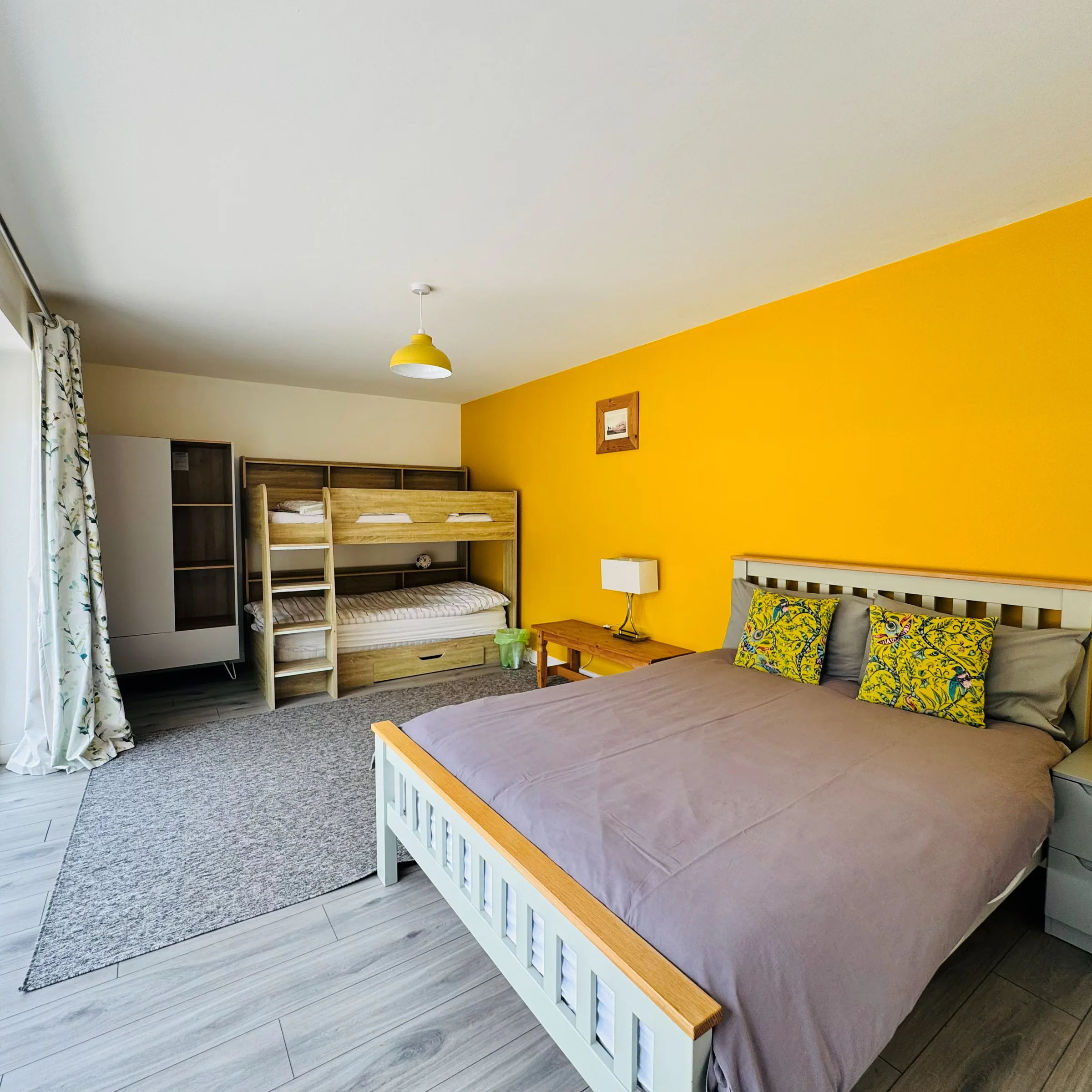 A Mordros bedroom with a double bed against a mustard-yellow feature wall and a wooden bunk bed alongside