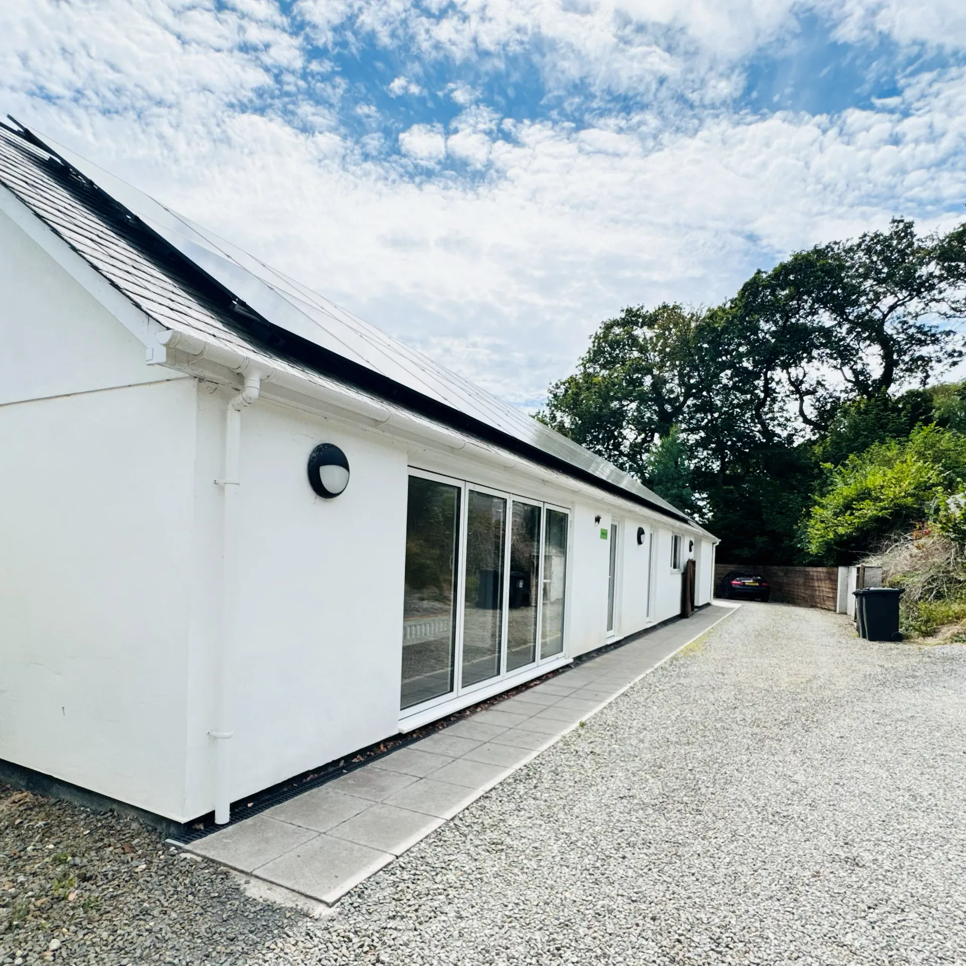The long white single-storey Mordros lodge, solar panels along its slate roof and sliding patio doors opening onto a gravel drive