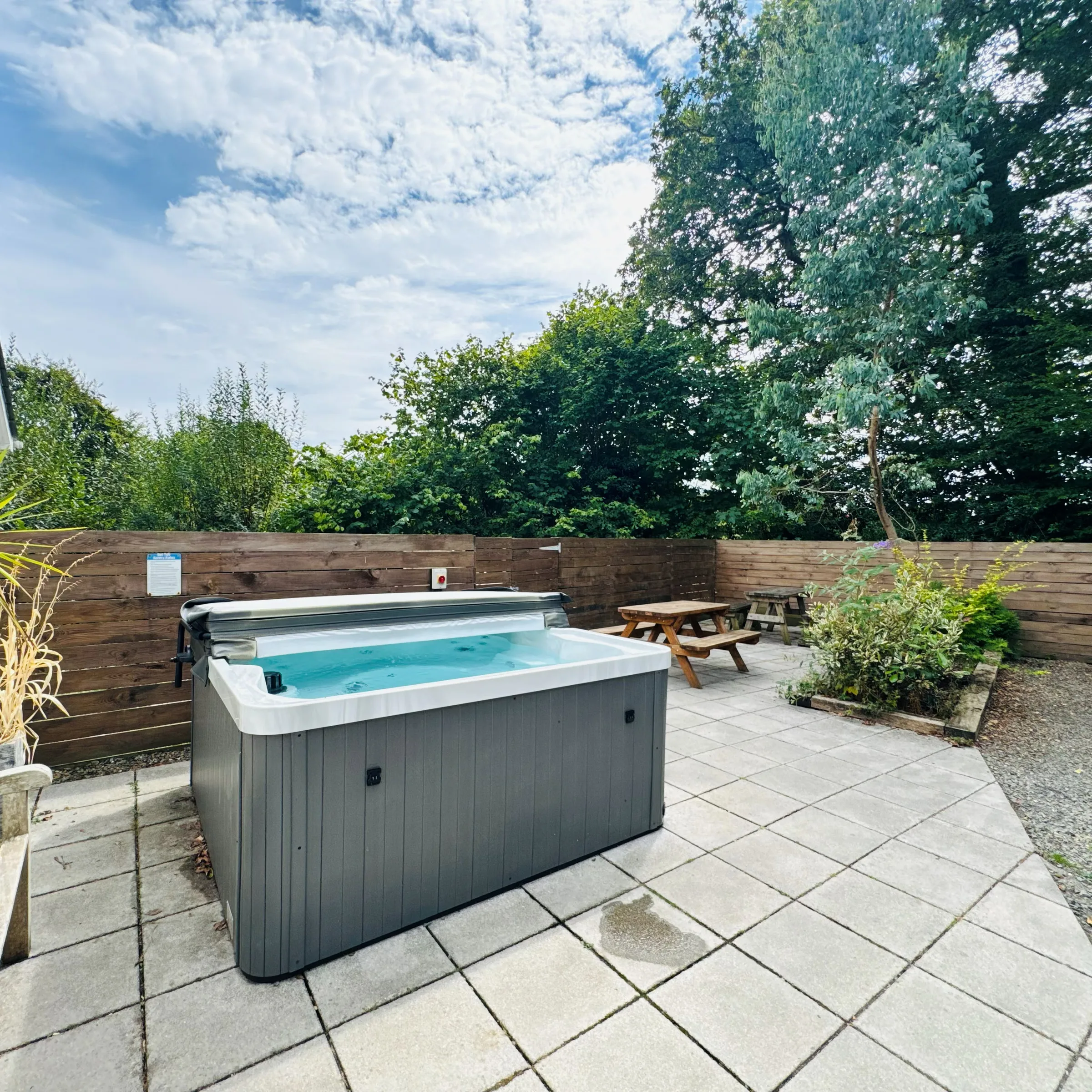 Mordros’s private hot tub on the paved patio, with a picnic table and fenced garden behind