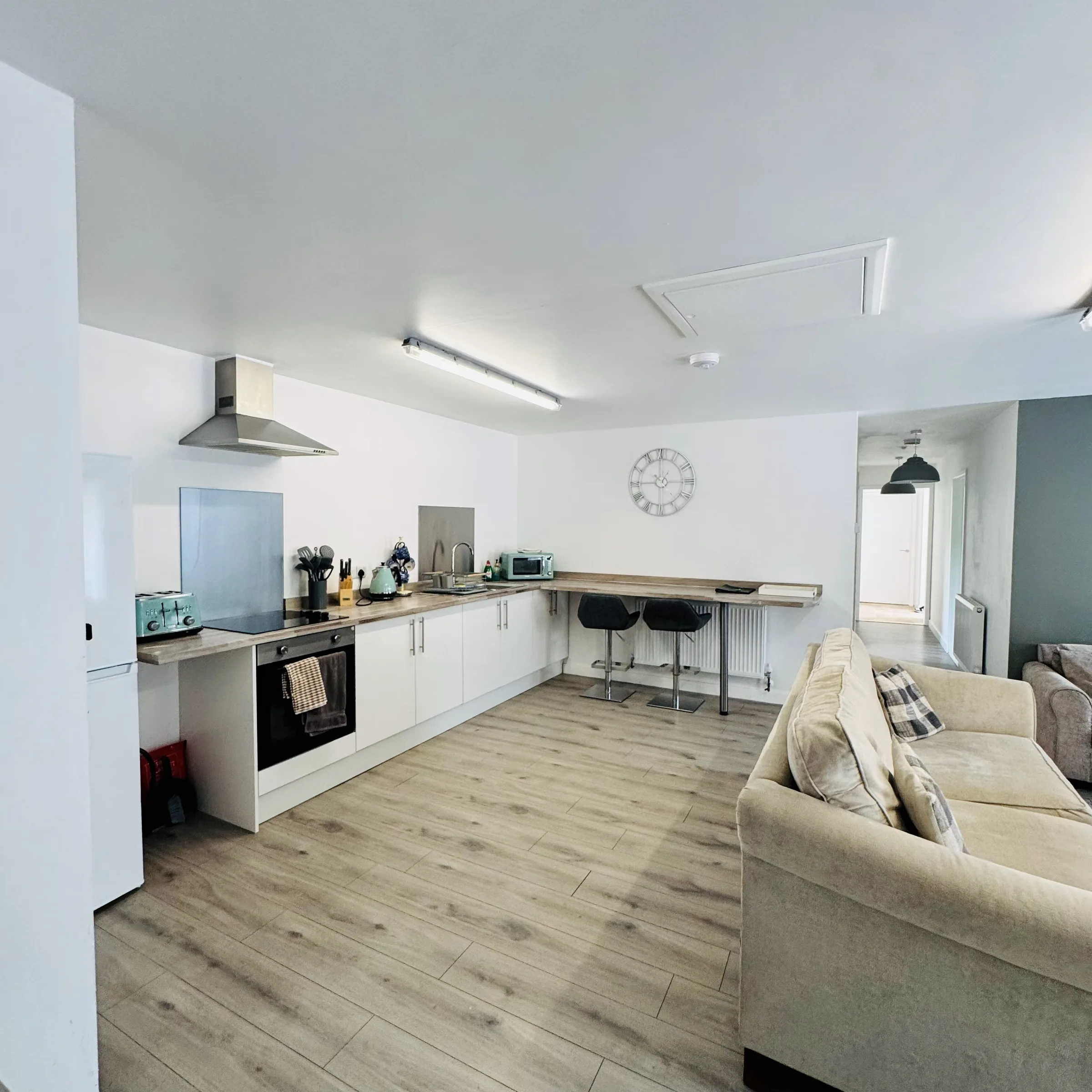 The kitchen at Mordros, white units and a wood-topped breakfast bar with stools, opening straight onto the lounge