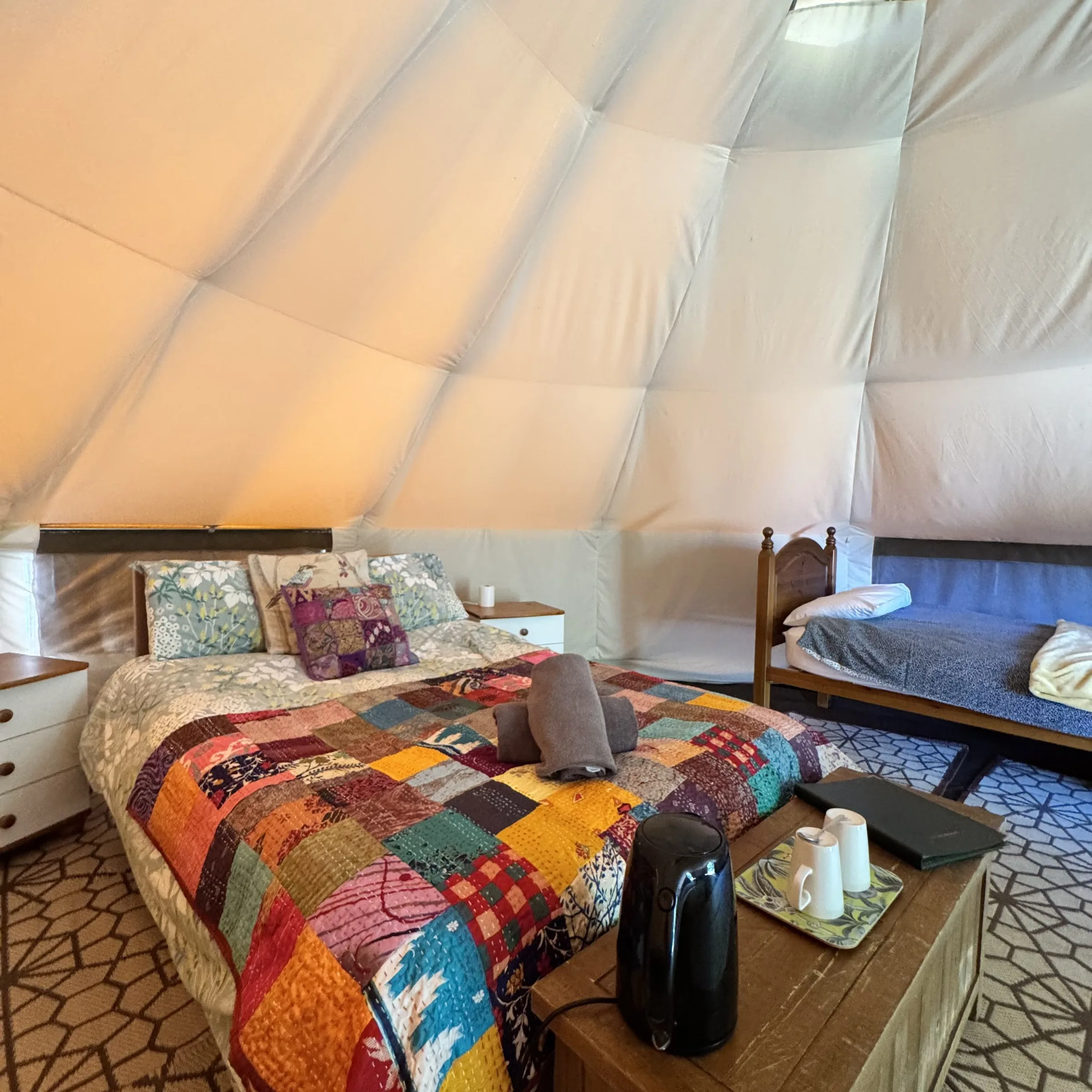A double bed under a patchwork quilt in one of our bell tents, with the kettle and guest folder on the table alongside