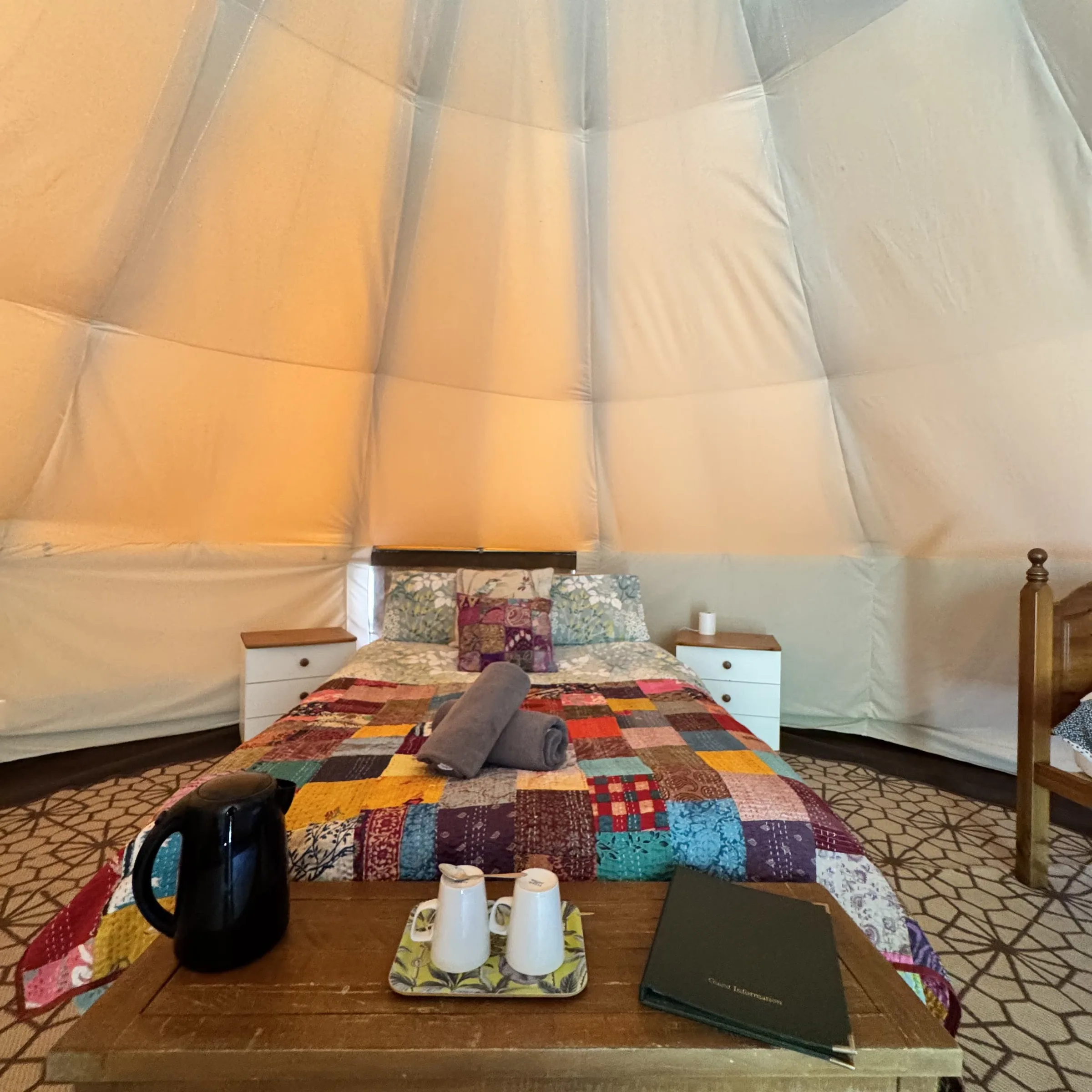 The double bed and a single bed inside one of our bell tents, made up under a patchwork quilt with the kettle and tray on the table