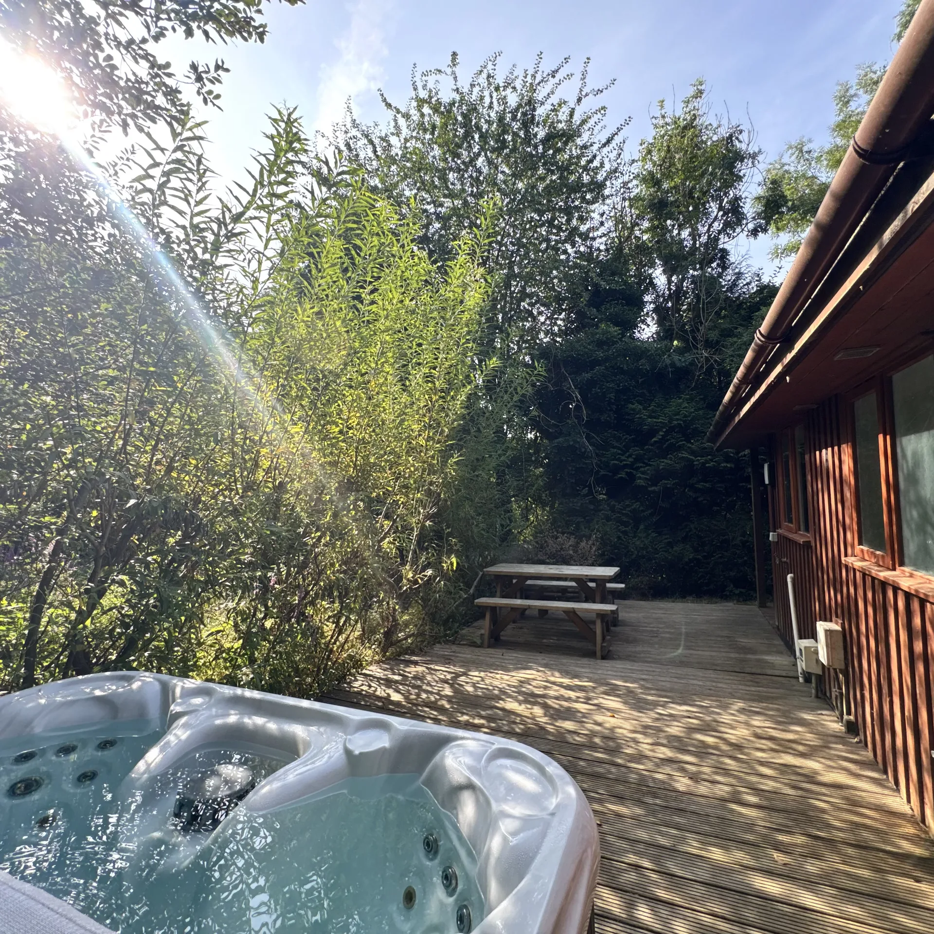 The hot tub on Stamford’s deck in dappled woodland light, with the lodge behind