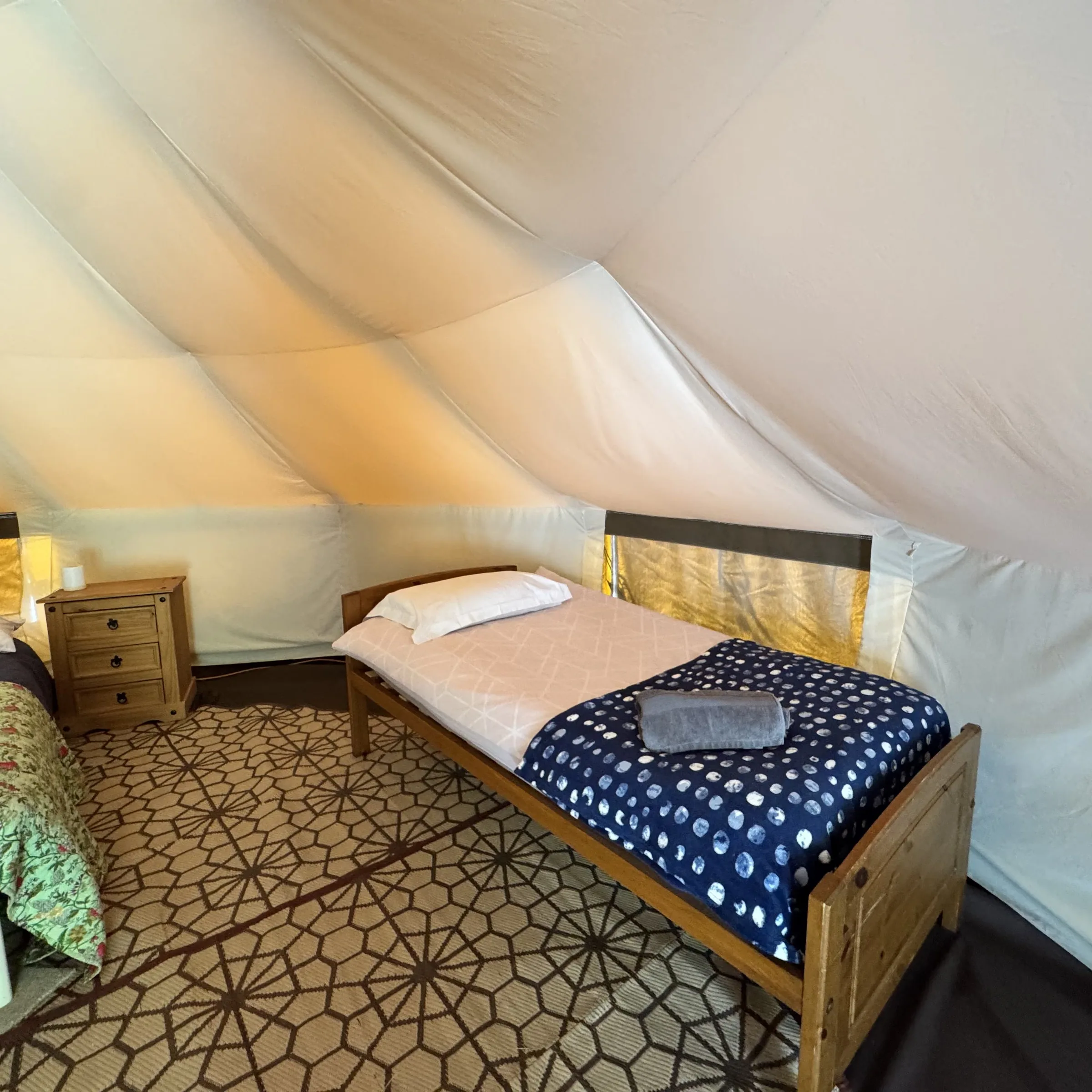 The single bed at St Enodoc under the sloping canvas wall, with a warm lamp lit alongside