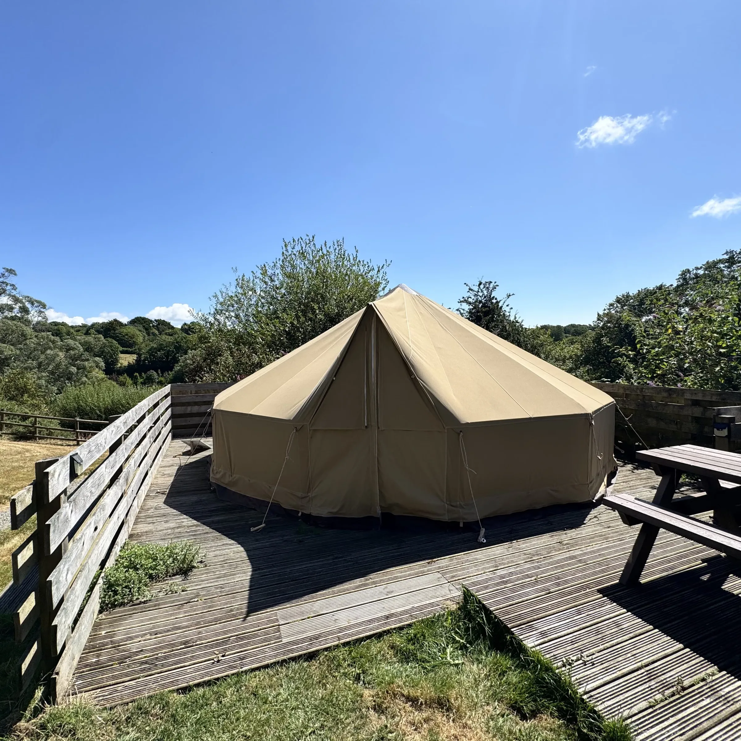 St Enodoc’s bell tent on its timber deck, with the picnic bench alongside and countryside beyond
