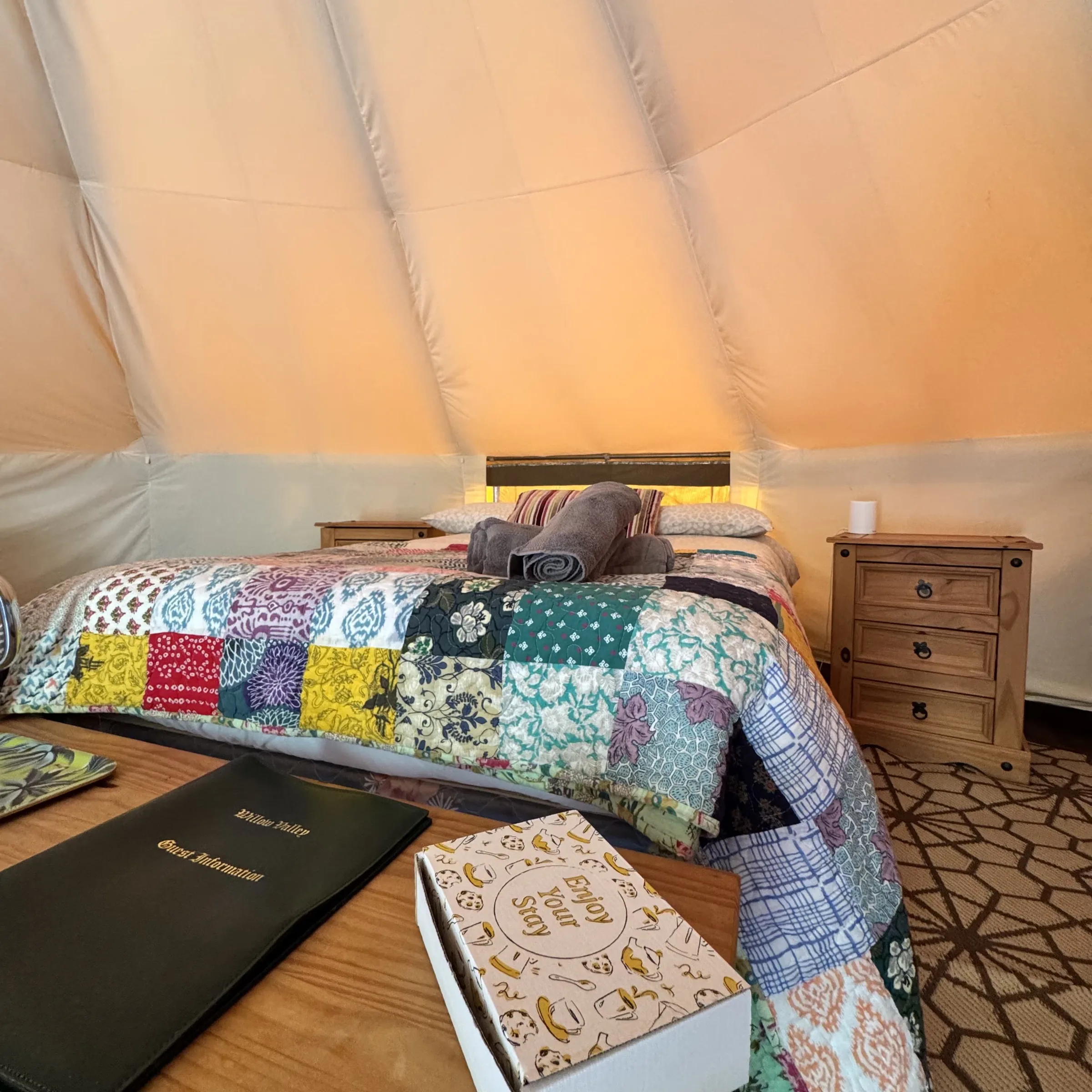 The double bed at St Petroc, made up with a patchwork quilt, rolled towels and the guest welcome box